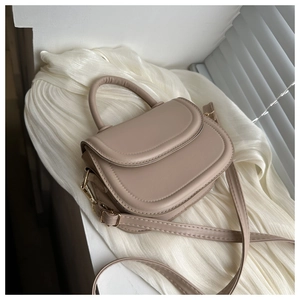 Detail of minimalist cream saddle bag featuring a smooth leather finish and metallic gold hardware