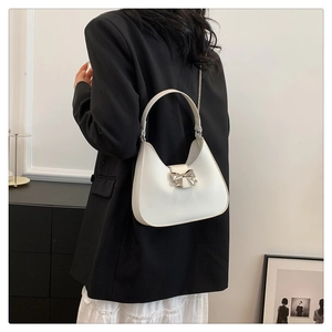 Close-up of white hobo bag with silver bow accent and metal chain on a model