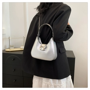 Detail of silver bow-knot handbag with metallic chain strap worn over a black blazer