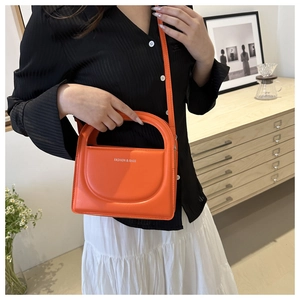 Detail of bright orange faux leather bag with white text on a black outfit background