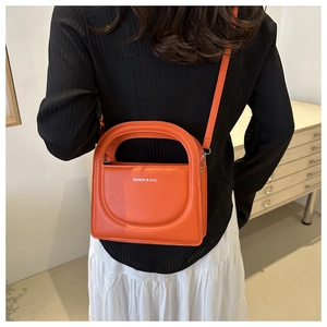 Detail shot of a bright orange crossbody bag featuring white fashion letters and top handle