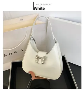 Detail of white half-moon shoulder bag featuring a silver metal bow buckle on the front