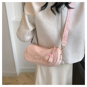 Detail of pink nylon cylinder crossbody bag with wide shoulder strap worn by a model