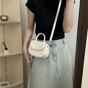Minimalist cream saddle crossbody bag with top handle shown on a model in a casual outfit