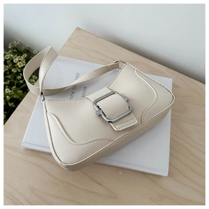 Detail of cream PU leather baguette bag with silver buckle on a wooden table with daisies