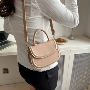 Minimalist beige PU leather saddle bag with round handle and gold-tone strap on a model