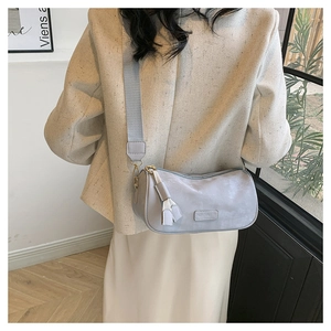 Close-up of light blue cylinder crossbody bag with wide strap and tassel detail