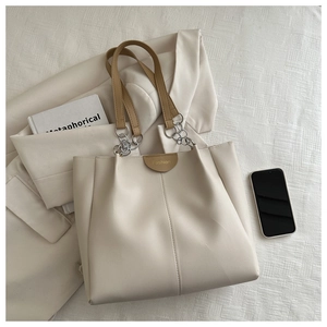 Detailed shot of a cream tote bag with brown straps, fashion plaque, and metal chain