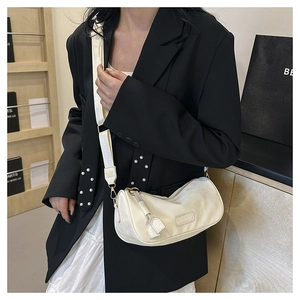 Close-up of cream crescent crossbody bag with wide strap and leather tassel detail