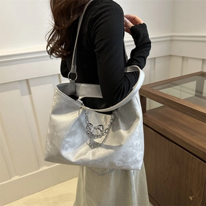 Silver metallic tote bag with chain strap and bow charm on a model in a minimal setting