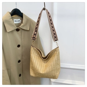 Detail of woven straw tote bag featuring a colorful geometric embroidered shoulder strap
