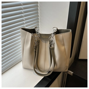 Detail of cream tote bag with accordion pleats, green leather trim and silver chain strap