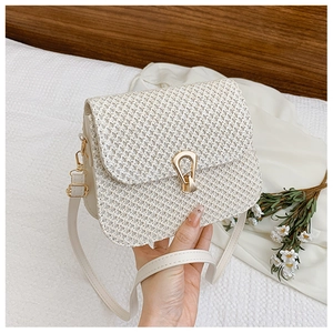 Close-up of white woven straw crossbody bag with golden horseshoe buckle and strap