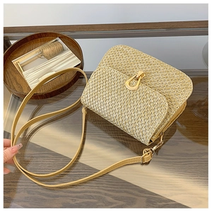 Detail of the woven straw texture and gold teardrop clasp on a beige crossbody bag