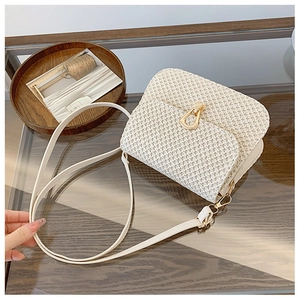 Detail of cream woven straw bag featuring a golden horseshoe buckle and fine textures