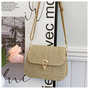 Detail of straw woven crossbody bag featuring a golden horseshoe buckle and slim strap