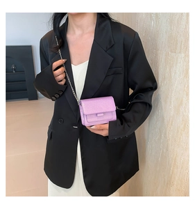 Détail d'un sac bandoulière violet à paillettes avec chaîne argentée sur blazer