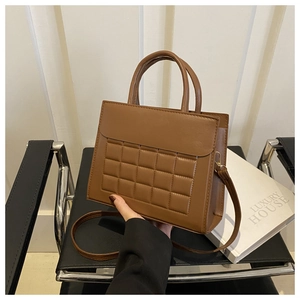 Dettaglio di una borsa tote marrone trapuntata con doppi manici e una tracolla lunga