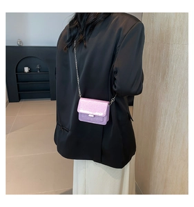 Petit sac carré rose pailleté avec bandoulière chaîne porté sur veste noire et jupe beige