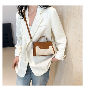 Detail of a brown leather and beige straw patchwork crossbody bag on a model
