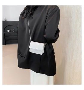 Détail d'un sac bandoulière à paillettes blanches avec chaîne argentée sur blazer noir