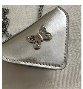 Vue détaillée du sac triangle argenté avec boucle papillon ajourée et bandoulière chaîne