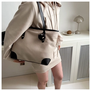 Detalle del bolso tote de lona crema con bordes de cuero negro y colgante de felpa