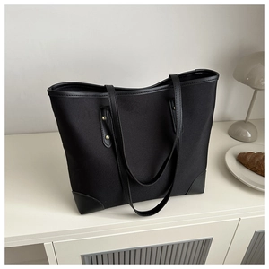 Detalle de bolso tote negro con ribete de cuero y remaches dorados en fondo blanco
