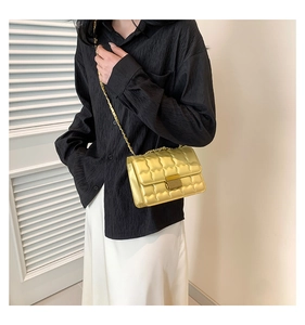 Detail of a golden quilted small square bag with chain strap on a black shirt
