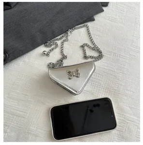 Mini sac triangle argenté avec chaîne et papillon comparé à la taille d'un téléphone