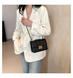 Detailed view of black quilted crossbody bag with gold metal lock and chain strap