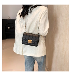 Detailed view of black quilted leather shoulder bag with golden lock on a female model