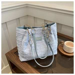 Close-up of light blue textured tote bag with golden chain handle and branded label