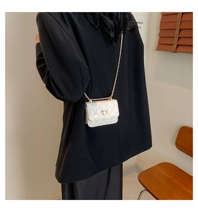 Detail of white quilted crossbody bag with gold chain strap on black blazer outfit