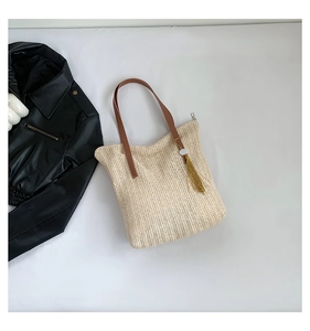 Vue détaillée d'un sac cabas en paille tressée avec lanières en cuir brun et glands jaunes