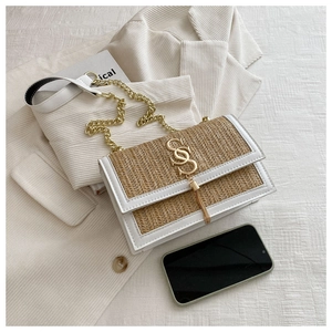 Detail of woven straw shoulder bag featuring gold S logo and elegant metal chain strap
