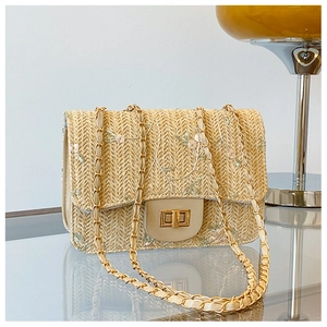 Close-up of beige straw bag with pink floral embroidery and golden twist lock closure