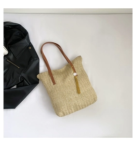 Détail du sac cabas en paille tressée avec anses en cuir et pompon en soie jaune