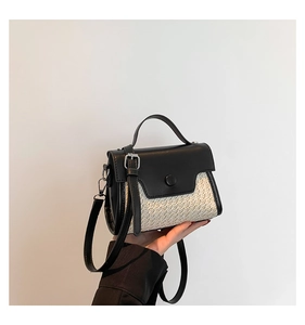 Detail of mini straw and black leather patchwork bag held by hand on white background