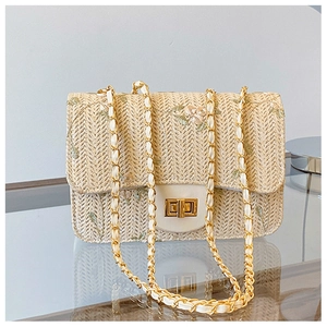 Detail of woven straw shoulder bag featuring embroidered floral patterns and gold chain