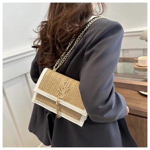 Detail of woven straw shoulder bag with metallic logo and chain strap on grey blazer