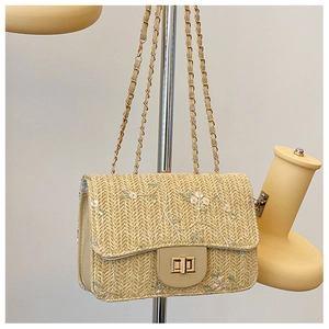 Detail of floral embroidery and gold metal clasp on a woven straw crossbody bag