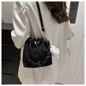 Détail du sac seau noir à cordon avec texture plissée et breloque chiot en peluche blanche