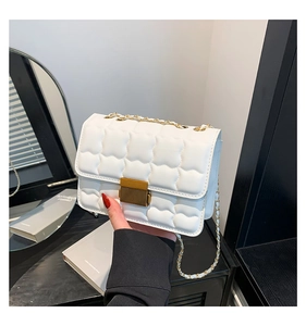 Close-up of white quilted crossbody bag featuring gold metal chain and rectangular lock