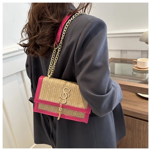 Detail of a straw crossbody bag with pink leather trim and gold chain on a female model