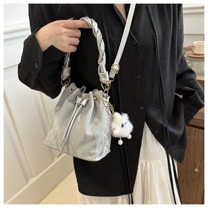 Détail du sac seau argenté avec texture plissée et charme de boule en peluche blanche