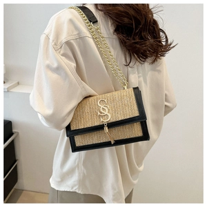 Detail of woven straw handbag with black leather trim and gold chain strap shown on model