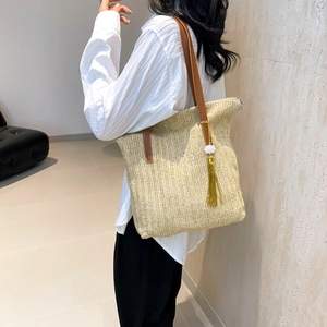 Femme portant un sac cabas en paille tressée avec bandoulière en cuir et gland jaune