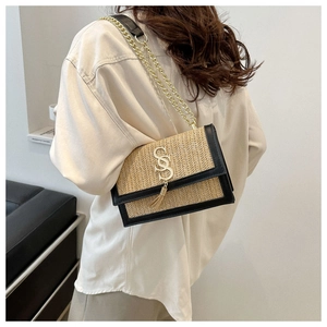 Detail of woven straw shoulder bag with gold letter S hardware and leather trim