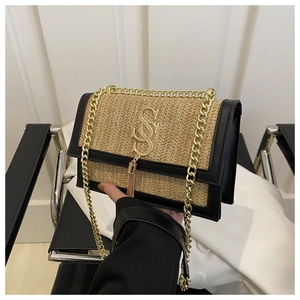 Close-up of woven straw handbag with black leather trim and gold metal logo charm